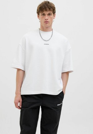 Hvid oversized t-shirt lavet af blødt bomuld med korte ærmer, med et lille "CORE CREATIVE" logo og parret med sorte cargo-bukser.