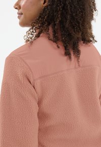 Lichtroze fleece jacket met een textuur, fluffy lichaam en een glattere, effen stof in het schoudergedeelte. Beschikt over een hoge kraag en gestikte details.