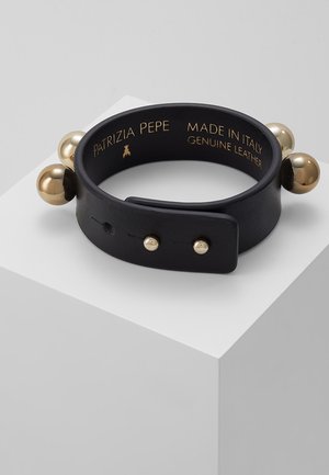 Musta aito nahkaranneke kultaisen sävyisillä niiteillä ja palloilla, jossa teksti "Patrizia Pepe Made in Italy", esillä valkoisella jalustalla.