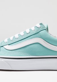 Baskets en toile bleu clair avec des lacets blancs, une bande latérale blanche et une semelle en caoutchouc texturée avec une ligne d'accent noire.