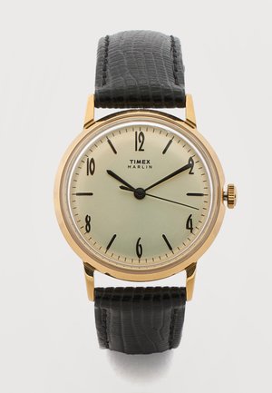 Timex Marlin -rannekello, jossa on kultainen kotelo, kerma kellotaulu, mustat arabialaiset numerot ja musta teksturoitu nahkaranneke, ajanäkymä 10:10:15.