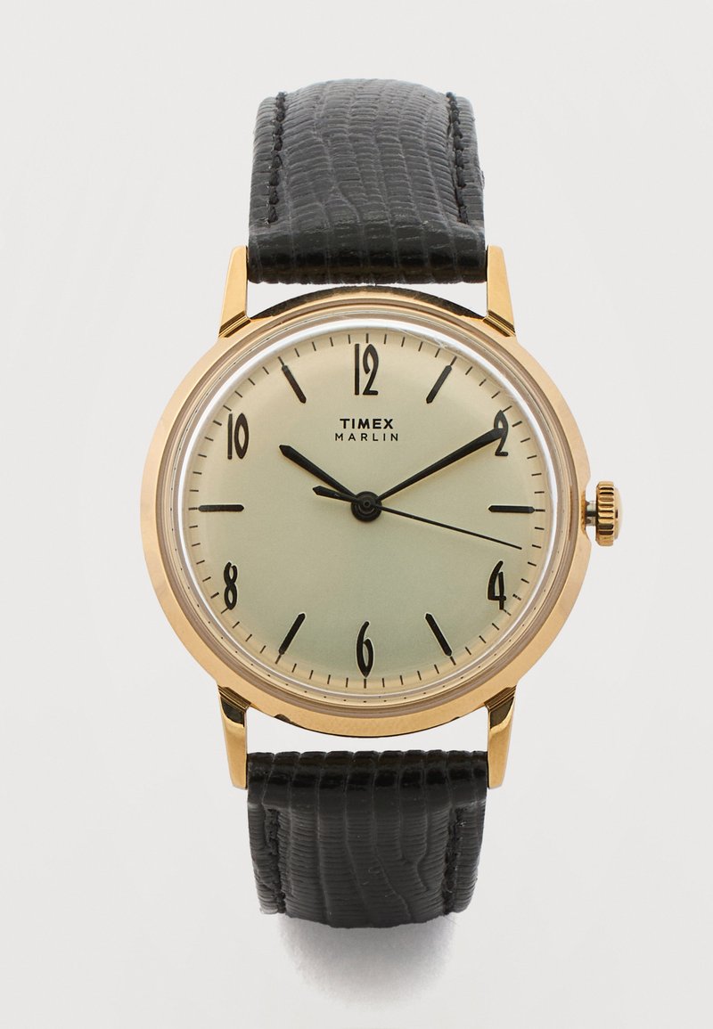Ρολόι χειρός Timex Marlin με χρυσαφένια θήκη, κρεμ καντράν, μαύρους αραβικούς αριθμούς και μαύρο δερμάτινο λουράκι με υφή, δείχνει 10:10:15.