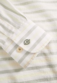 Tessuto della camicia leggermente strutturato con strisce bianche e grigie chiare. Presenta un polsino piegato con due bottoni, uno verde e uno crema.