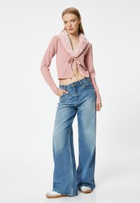 Rippierter rosa Crop-Top mit einem Kunstfellkragen und vorn gebunden, kombiniert mit einer hochtaillierten, weiten blauen Jeans und weißen Sneakers.