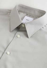 Hellgraues Slim-Fit-Hemd mit strukturiertem Kragen, texturiertem Stoff, drei Knöpfen und einem Markenlabel im Kragen.
