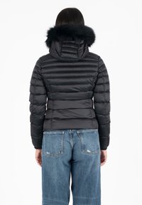 Giubbotto imbottito nero con cappuccio foderato in pelliccia, caratterizzato da un design trapuntato e polsini a coste, abbinato a jeans a gamba larga di un blu chiaro.