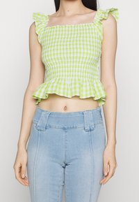 Zelený a bílý kostkovaný crop top s nařaseným designem, čtvercovým výstřihem a volánkovými ramínky. V kombinaci s modrými džíny s vysokým pasem.