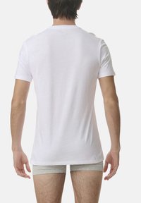 White cotton T-shirt with a crew neckline, visible stitching, and short sleeves, worn with gray boxer briefs. Back view shows smooth texture.