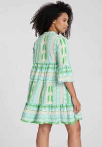 Vestido verde y azul con un patrón, mangas de tres cuartos, volantes en capas y una silueta fluida. Tela de algodón con diseños geométricos.