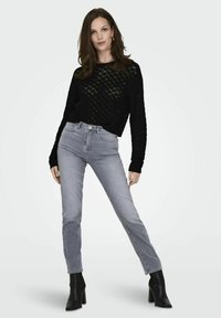 Černý pletený svetr s diamantovým vzorem, spárovaný s světle šedými džíny s vysokým pasem a černými koženými kotníkovými botami na podpatku.