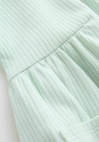 Tissu côtelé vert clair avec une couture horizontale pliant le matériau en plis froncés au centre.