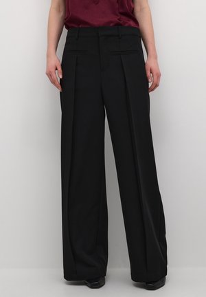 Woman wearing high-waisted, wide-leg black trousers with front pleats and back welt pockets, paired with a burgundy sleeveless top.