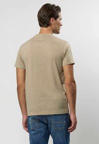 Beež lühikeste varrukatega T-särk ümarate kaelustega, valmistatud tekstuurse kangaga. Kantud siniste teksapükstega, näidates lõdvestatud istuvust.