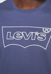 Námořnická modrá bavlněná tričko s velkým bílým logem Levi's a ochrannou známkou, s designem klasického kulatého výstřihu a jemnou texturou.