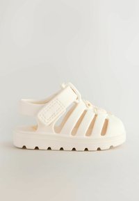 Kids’ white closed-toe sandal with adjustable strap and thick tread sole, shown on a plain light background.