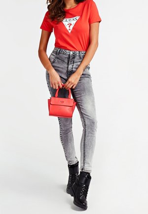 Rød Guess T-shirt med logo, grå jeans og en rød taske med præget logo. Sorte militærstøvler med snøre og syningsdetaljer på jeansene.