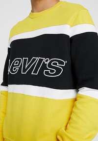 Žlutá, černá a bílá mikina s výrazným logem "Levi's". Vyrobena z měkké bavlny, s kulatým výstřihem a designem v barvách.