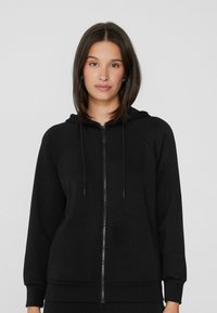 Černá mikina na zip s kapucí na stahování, raglánovými rukávy, žebrovanými manžetami a spodním lemem a hladkým povrchem. Jednoduchý design bez vzorů.