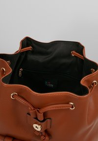 Braune Leder-Eimer Tasche mit einem Kordelzugverschluss, goldenen Hardware-Akzenten und einem schwarzen Stofffutter mit einer Reißverschlusstasche im Inneren.