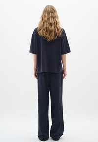 Laza szabású, sötét tengerészkék, rövid ujjú felső, széles lábú, sötét tengerészkék nadrággal párosítva, mindkettő puha, texturált anyagból készült.