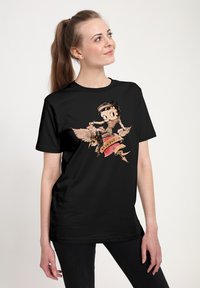 Camiseta de algodón negra que presenta un gráfico de estilo vintage de un personaje con alas en una pancarta que dice "Valor".