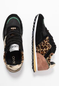 Svarta sneakers med leopardmönster, mockadetaljer i tan och grön, snörningsdesign och en vit kontrastsula med texturerat grepp.