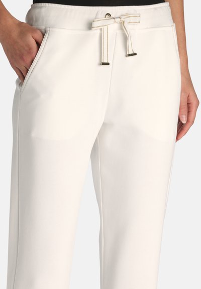 Pantalon décontracté blanc avec poches avant et taille à cordon noué, porté par une personne dont les mains reposent près des poches.