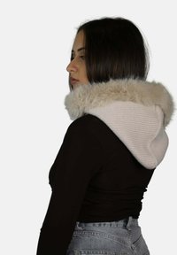 Felpa beige lavorata a maglia con interno morbido e peloso intorno al cappuccio; design aderente e trama senza cuciture; indossata con una maglietta nera e jeans blu.