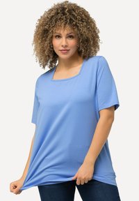 Blauw T-shirt met korte mouwen en een vierkante halslijn, gemaakt van zachte stof. Het heeft een losse pasvorm en is gecombineerd met donkerblauwe spijkerbroek.