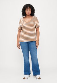  camiseta de cuello en V a rayas en color beige y blanco, de mangas cortas, combinada con jeans acampanados azules y zapatillas blancas. Ajuste casual y cómodo.