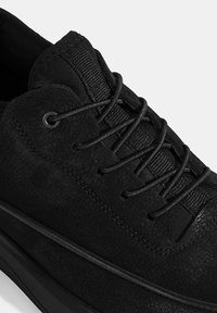Black sneaker featuring a textured suede upper, round laces, reinforced eyelets, and a contrasting rubber sole along the lower edge.