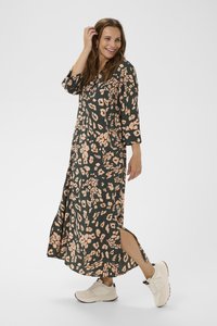 Maxi dress in dark green fabric with a pink leopard print, featuring three-quarter sleeves, side slits, and worn with light-colored sneakers.