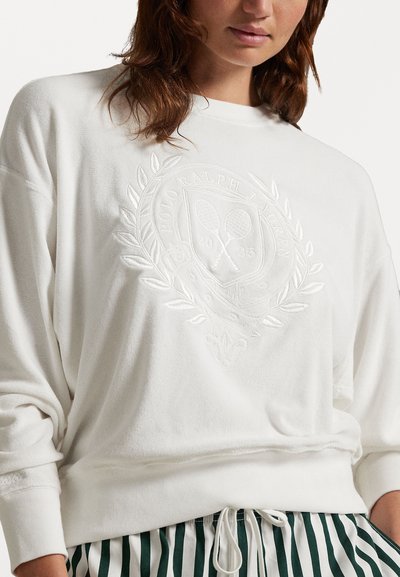 Hvit sweatshirt med preget logo og laurbærdesign. Har lange ermer og en litt cropped passform. Bæres med grønne og hvite stribede bukser.