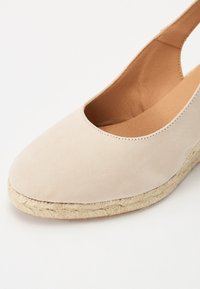 Beežist sueded espadrill jalats, ümarate varvastega, elastse külje ja kudumise jute tallaga. Pehme tekstuur ja minimalistlik disain.