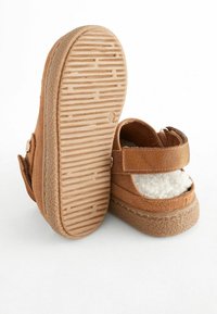 Sandales en daim marron avec une semelle en caoutchouc texturée, une sangle velcro et un doublure douce. Forme arrondie avec un design à bout ouvert et un talon découvert.