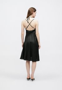 Μαύρο σατέν φόρεμα με τιράντες που διασταυρώνονται στην πλάτ�η, φαρδύ τελείωμα και απαλή υφή. Μήκος κάτω από το γόνατο με ελάχιστες λεπτομέρειες.