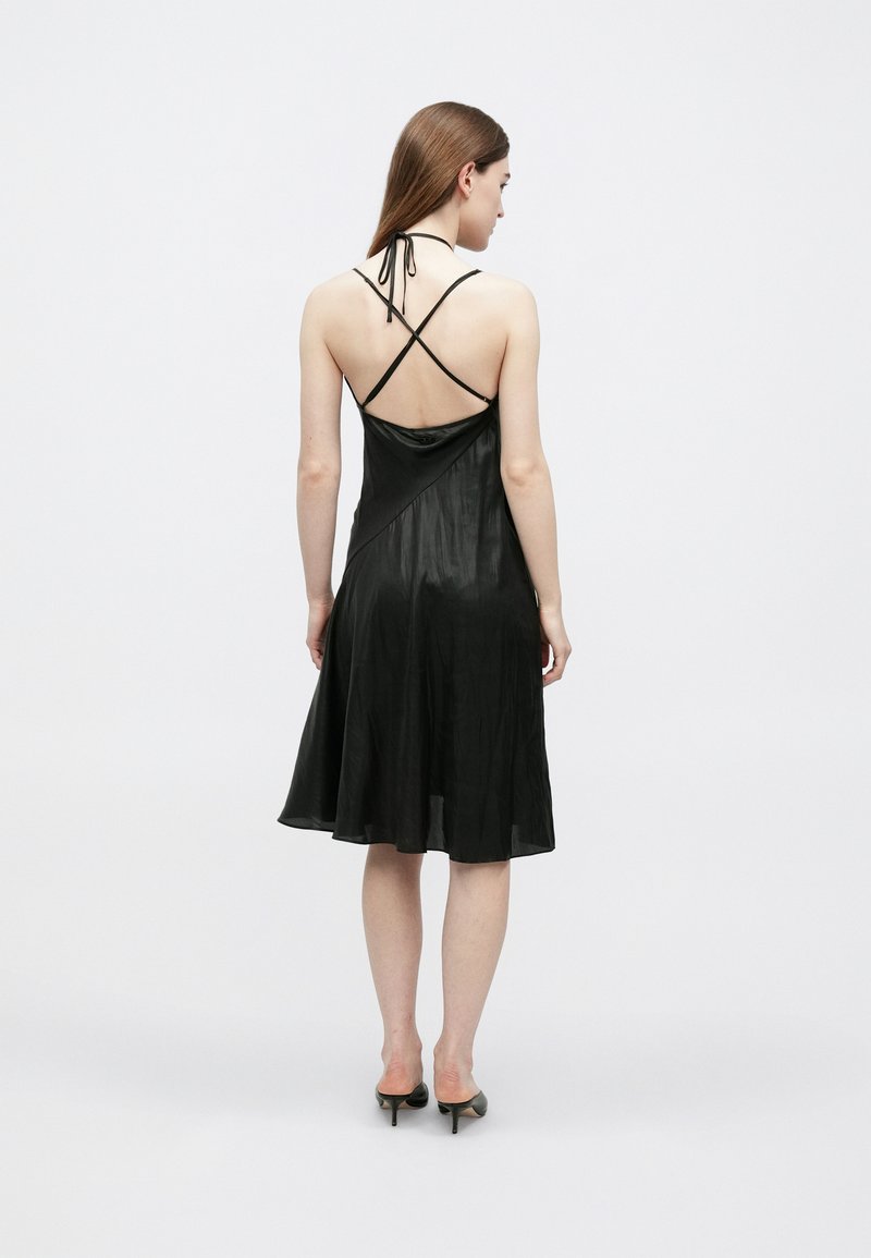 Sort satin-natkjole med krydsryg-stropper, skørt med bredde og blød tekstur. Længde under knæet med minimal detaljering.