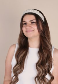 Fascia per capelli di perline composta da perle bianche e perline, con una fascia flessibile. Il modello ha lunghi capelli castani wave e indossa una maglietta bianca.