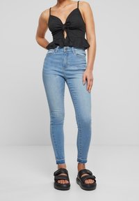 Black ribbed top with a knotted front and peplum hem, paired with light blue skinny jeans and black platform sandals.