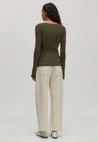 Olivgrünes, geripptes Langarmshirt, kombiniert mit off-white weit geschnittenen Hosen und silbernen Slippern, von hinten betrachtet.