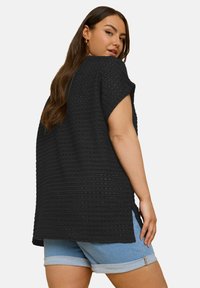 Black textured top featuring a loose fit, wide sleeves, and side slits, paired with light blue rolled denim shorts.