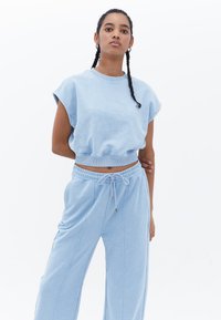 Sudadera corta de color azul claro con mangas cortas, cuello acanalado y pantalones de chándal a juego con cordón que presentan detalles de costura lateral.