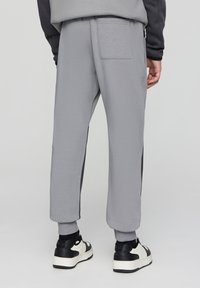 Szare dresowe spodnie o zwężanym kroju, z ciemnymi bocznymi panelami i tylną kieszenią. Gładka tekstura; ściągacze na kostkach.