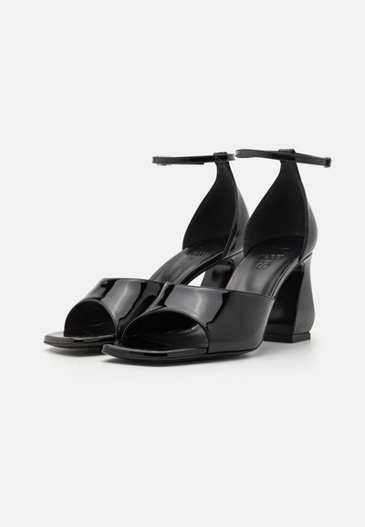 Black patent leather high-heeled sandals with an open toe and ankle strap. Square heel and smooth, glossy finish.