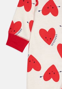 Piros és krém hosszúujjú ruhadarab játékos szívmintával, mosolygó arcokkal, nyíl részletekkel és piros mandzsettákkal.