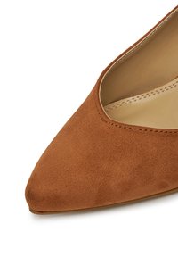 Barna velúr, hegyes orrú cipő sima felülettel és minimális varrással. Oldalain ívelt kivágásokkal tervezve, hogy elegáns megjelenést nyújtson.