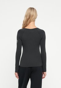 Top aderente a maniche lunghe di colore grigio scuro con una texture a coste e scollatura rotonda, dotato di maniche raglan e un logo sottile sulla spalla sinistra.