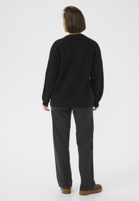 Schwarzer, flauschiger Pullover mit überschnittenen Schultern, kombiniert mit dunkelgrauen, geraden Hosen und braunen Schuhen. Minimalistisches Design auf einem schlichten weißen Hintergrund.