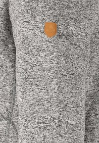 Grå strikket sweater med et tekstureret mønster og et lille logo af brunt læder på den øverste side. Justeret pasform med rund halsudskæring.