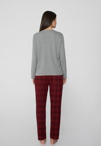 Top gris de manga larga con cuello redondo, combinado con pantalones de cuadros rojos. La tela parece suave y los pantalones tienen una cintura elástica.